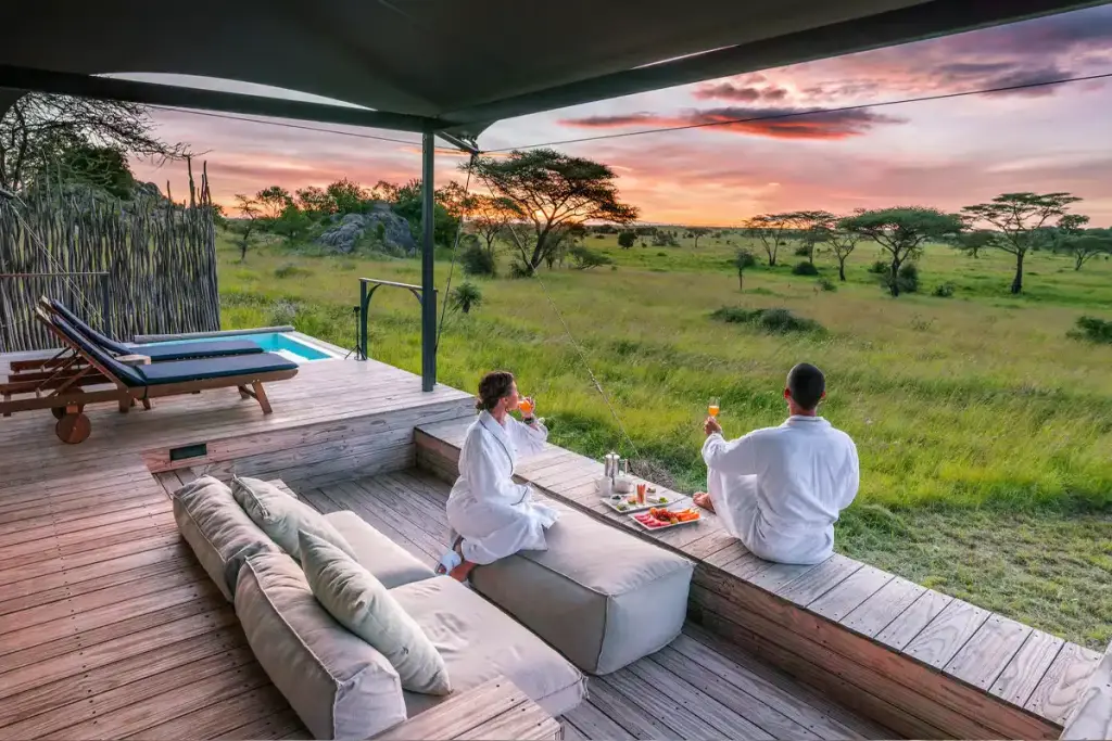 A couple on a lodge deck looking out over the savannah at sunset