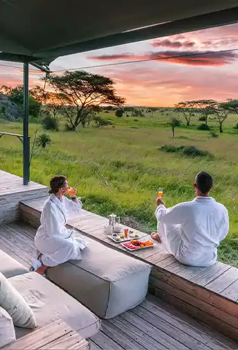 A couple in robes having breakfast on a lodge deck overlooking the savannah