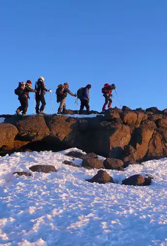 Climbers standing on a rocky ledge above the snow on Kilimanjaro